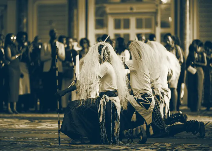 Intore dancers kneeling in a ballroom while guests watch